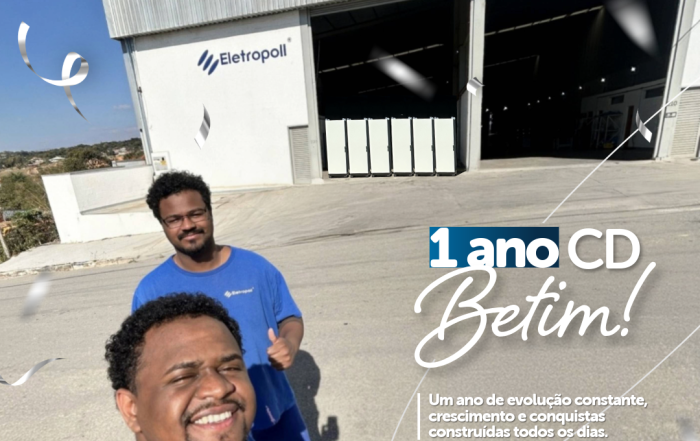 Dois colaboradores sorrindo em frente à fachada do Centro de Distribuição da Eletropoll em Betim (MG), com o texto '1 ano CD Betim!' sobreposto.